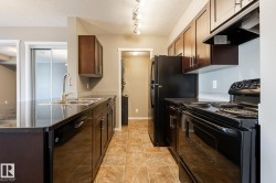 Kitchen with black appliances, range hood, a textured ceiling, a peninsula, and dark stone countertops - 