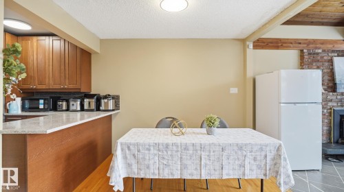 Kitchen featuring freestanding refrigerator, wood finish cabinets, light stone counters, a textured ceiling, and black microwave - 11520 78 Avenue Nw, Edmonton, AB - Indoor Photo Showing Kitchen