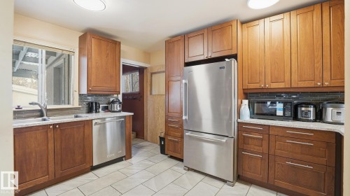 Kitchen featuring tasteful backsplash, stainless steel appliances, wood finish cabinetry, and light stone counters - 11520 78 Avenue Nw, Edmonton, AB - Indoor Photo Showing Kitchen With Double Sink