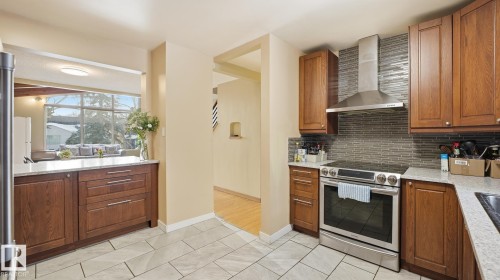 Kitchen featuring stainless steel electric stove, light stone counters, wood finish cabinetry, backsplash, and light tile patterned flooring - 11520 78 Avenue Nw, Edmonton, AB - Indoor Photo Showing Kitchen