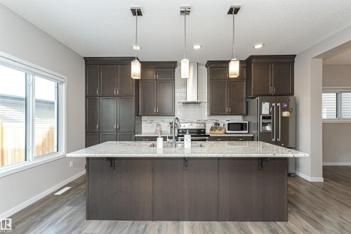 Kitchen featuring dark wood finish cabinets, a breakfast bar area, light stone counters, stainless steel appliances, and a textured ceiling - 4008 Allan Crescent, Edmonton, AB - Indoor Photo Showing Kitchen With Upgraded Kitchen