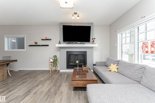 Living room with wood finished floors, a glass covered fireplace, and a textured ceiling - 4008 Allan Crescent, Edmonton, AB - Indoor Photo Showing Living Room With Fireplace