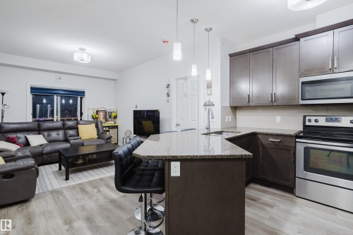 Kitchen with stainless steel appliances, dark stone countertops, open floor plan, dark wood finish cabinets, and a peninsula - 415 2203 44 Avenue, Edmonton, AB - Indoor Photo Showing Kitchen With Stainless Steel Kitchen With Upgraded Kitchen
