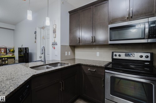 Kitchen featuring stainless steel appliances, light stone countertops, dark wood finish cabinets, tasteful backsplash, and decorative light fixtures - 415 2203 44 Avenue, Edmonton, AB - Indoor Photo Showing Kitchen With Double Sink With Upgraded Kitchen