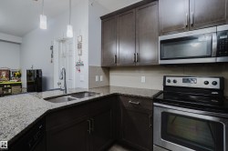 Kitchen featuring stainless steel appliances, light stone countertops, dark wood finish cabinets, tasteful backsplash, and decorative light fixtures - 