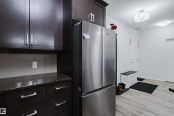 Kitchen featuring freestanding refrigerator, dark stone countertops, dark wood finish cabinetry, light wood finished floors, and a textured ceiling - 