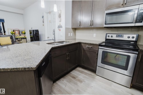 Kitchen featuring stainless steel appliances, light stone countertops, light wood finished floors, a peninsula, and backsplash - 415 2203 44 Avenue, Edmonton, AB - Indoor Photo Showing Kitchen With Stainless Steel Kitchen With Double Sink