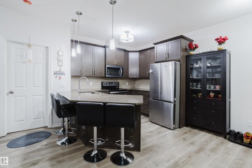 Kitchen with stainless steel appliances, a peninsula, a kitchen bar, pendant lighting, and light wood-style floors - 415 2203 44 Avenue, Edmonton, AB - Indoor Photo Showing Kitchen With Stainless Steel Kitchen
