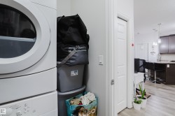 Laundry area featuring stacked washer and dryer, light wood-style floors, and a textured ceiling - 