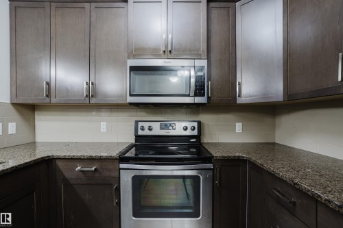Kitchen featuring stainless steel appliances, dark stone counters, dark wood finish cabinetry, and decorative backsplash - 415 2203 44 Avenue, Edmonton, AB - Indoor Photo Showing Kitchen