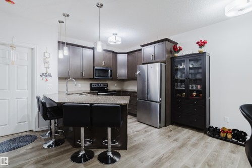 Kitchen with stainless steel appliances, a breakfast bar, a peninsula, decorative light fixtures, and dark wood finish cabinets - 415 2203 44 Avenue, Edmonton, AB - Indoor Photo Showing Kitchen With Stainless Steel Kitchen