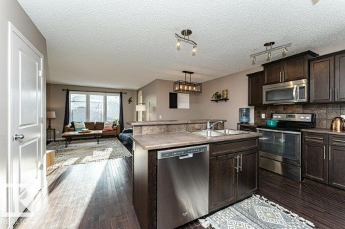 Kitchen featuring stainless steel appliances, dark wood finish cabinets, tasteful backsplash, rail lighting, and a center island with sink - 6649 Cardinal Road Sw, Edmonton, AB - Indoor Photo Showing Kitchen With Stainless Steel Kitchen With Double Sink