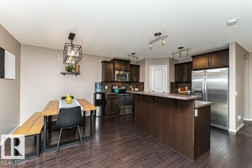 Kitchen with dark wood finish cabinets, stainless steel appliances, a breakfast bar area, pendant lighting, and a textured ceiling - 6649 Cardinal Road Sw, Edmonton, AB - Indoor Photo Showing Kitchen With Stainless Steel Kitchen