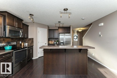 Kitchen with dark wood finish cabinetry, stainless steel appliances, tasteful backsplash, a breakfast bar, and dark wood-style floors - 6649 Cardinal Road Sw, Edmonton, AB - Indoor Photo Showing Kitchen