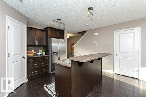 Kitchen with dark wood finish cabinetry, stainless steel fridge, rail lighting, a kitchen bar, and tasteful backsplash - 6649 Cardinal Road Sw, Edmonton, AB - Indoor Photo Showing Kitchen