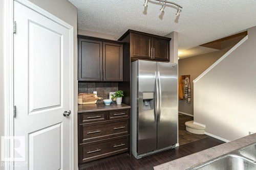 Kitchen with dark wood finish cabinetry, stainless steel fridge, dark wood-style floors, decorative backsplash, and track lighting - 6649 Cardinal Road Sw, Edmonton, AB - Indoor Photo Showing Kitchen