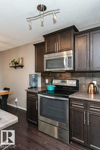 Kitchen featuring stainless steel appliances, dark wood finish cabinets, decorative backsplash, a textured ceiling, and rail lighting - 6649 Cardinal Road Sw, Edmonton, AB - Indoor Photo Showing Kitchen
