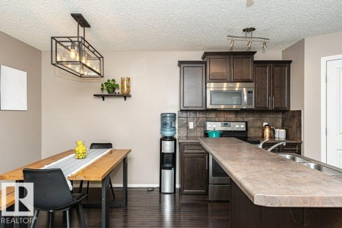 Kitchen with dark wood finish cabinets, stainless steel appliances, a textured ceiling, dark wood-style floors, and decorative backsplash - 6649 Cardinal Road Sw, Edmonton, AB - Indoor