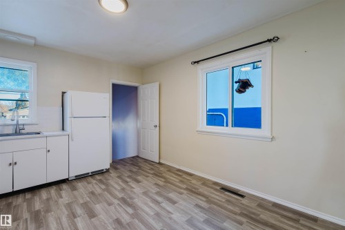 Kitchen featuring freestanding refrigerator, white cabinets, light wood-type flooring, light countertops, and tasteful backsplash - 10511 80 Street, Edmonton, AB 