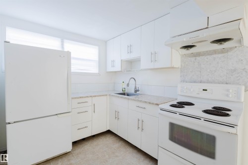 Kitchen with white appliances, white cabinetry, light countertops, and light tile patterned floors - 10511 80 Street, Edmonton, AB 