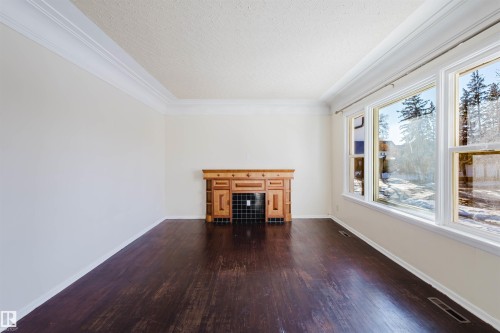 Unfurnished living room featuring a fireplace, dark wood-type flooring, crown molding, and a textured ceiling - 10511 80 Street, Edmonton, AB 