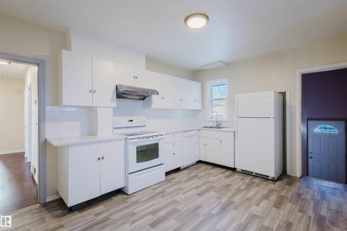 Kitchen featuring white cabinets, white appliances, light countertops, and exhaust hood - 10511 80 Street, Edmonton, AB 