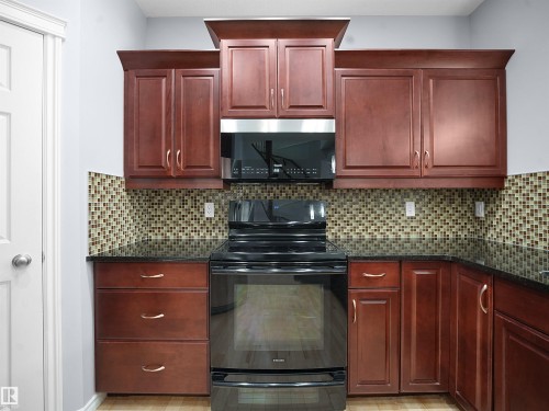 Kitchen with black range with electric stovetop, bold wood finish cabinets, dark stone countertops, and decorative backsplash - 6115 11 Avenue, Edmonton, AB - Indoor Photo Showing Kitchen
