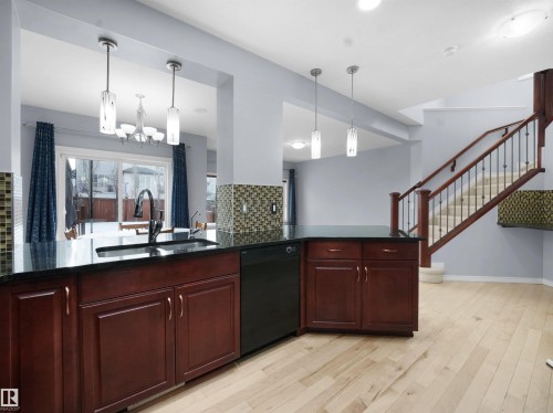Kitchen with bold wood finish cabinets, black dishwasher, decorative backsplash, light wood-style flooring, and suspended lighting - 6115 11 Avenue, Edmonton, AB - Indoor Photo Showing Kitchen With Double Sink