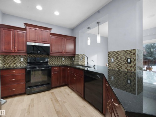 Kitchen with black appliances, bold wood finish cabinetry, dark stone countertops, pendant lighting, and light wood-style floors - 6115 11 Avenue, Edmonton, AB - Indoor Photo Showing Kitchen