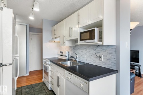 Kitchen with white appliances, a textured ceiling, dark countertops, backsplash, and white cabinetry - 304 9725 106 Street, Edmonton, AB - Indoor Photo Showing Kitchen