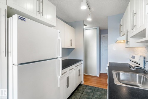 Kitchen featuring freestanding refrigerator, dark countertops, a textured ceiling, white cabinetry, and track lighting - 304 9725 106 Street, Edmonton, AB - Indoor Photo Showing Kitchen