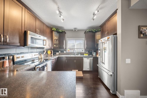 Kitchen with stainless steel appliances, dark countertops, dark wood finish cabinetry, glass insert cabinets, and dark wood-style floors - 8107 224 Street Nw, Edmonton, AB - Indoor Photo Showing Kitchen With Upgraded Kitchen