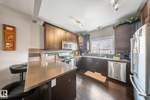 Kitchen featuring stainless steel appliances, a breakfast bar, dark countertops, a peninsula, and a textured ceiling - 8107 224 Street Nw, Edmonton, AB - Indoor Photo Showing Kitchen