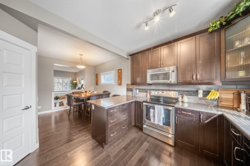 Kitchen with stainless steel appliances, a peninsula, glass fronted cabinets, decorative light fixtures, and a textured ceiling - 8107 224 Street Nw, Edmonton, AB - Indoor Photo Showing Kitchen