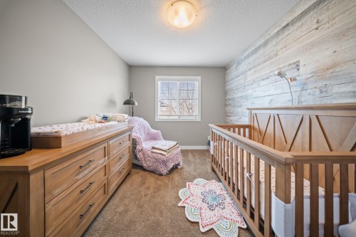 Carpeted bedroom with a crib, wood walls, and a textured ceiling - 8107 224 Street Nw, Edmonton, AB - Indoor Photo Showing Bedroom