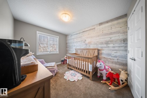 Bedroom featuring wooden walls, dark colored carpet, a nursery area, an accent wall, and a textured ceiling - 8107 224 Street Nw, Edmonton, AB - Indoor Photo Showing Bedroom
