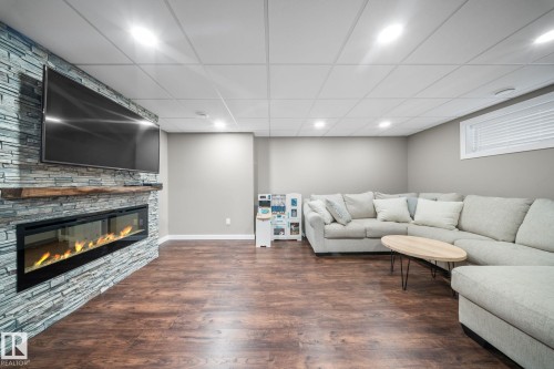 Living room featuring a drop ceiling, wood finished floors, a stone fireplace, and recessed lighting - 8107 224 Street Nw, Edmonton, AB - Indoor Photo Showing Basement With Fireplace