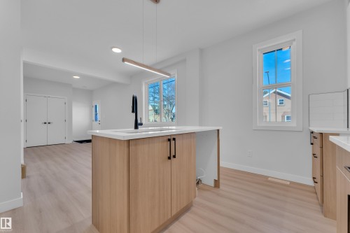Kitchen featuring pendant lighting, a center island with sink, light wood-style flooring, light stone counters, and two tone cabinets - 9531/ 9533 115 Ave, Edmonton, AB - Indoor Photo Showing Kitchen