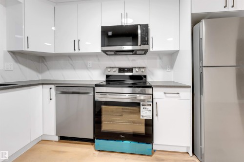 Kitchen featuring stainless steel appliances, white cabinets, dark stone countertops, light wood-type flooring, and modern cabinets - 7303 130 Avenue, Edmonton, AB - Indoor Photo Showing Kitchen With Upgraded Kitchen