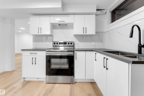 Kitchen featuring white cabinetry, stainless steel range with electric cooktop, light wood-style floors, dark stone counters, and recessed lighting - 7303 130 Avenue, Edmonton, AB - Indoor Photo Showing Kitchen With Double Sink With Upgraded Kitchen
