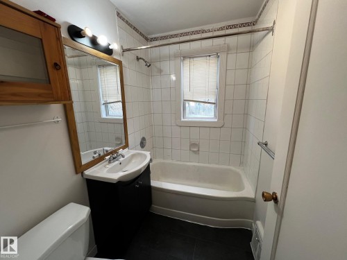 Bathroom featuring washtub / shower combination, vanity, and dark tile patterned floors - 10830 68 Avenue, Edmonton, AB - Indoor Photo Showing Bathroom