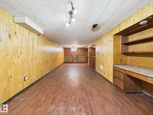 Finished basement featuring dark wood-style floors, built in study area, wood walls, and track lighting - 13523 124B Avenue, Edmonton, AB - Indoor Photo Showing Other Room