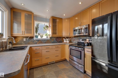 Kitchen with stainless steel appliances, light wood finish cabinets, dark stone finish floors, light countertops, and glass insert cabinets - 10911 66 Avenue, Edmonton, AB - Indoor Photo Showing Kitchen With Double Sink