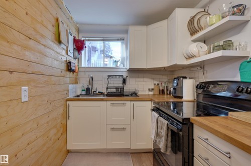 Kitchen featuring black range with electric stovetop, open shelves, white cabinetry, wooden counters, and light wood finished floors - 10911 66 Avenue, Edmonton, AB - Indoor Photo Showing Kitchen