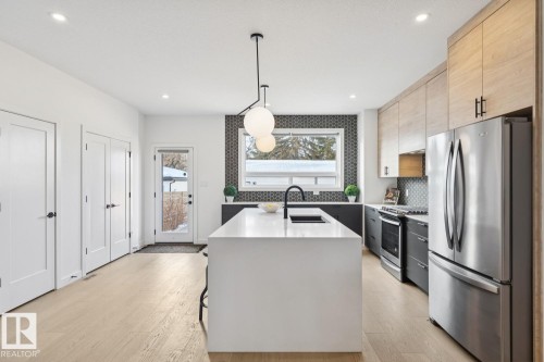 Kitchen with stainless steel appliances, hanging light fixtures, modern cabinets, light stone counters, and light wood-style floors - 11016 132 Street, Edmonton, AB - Indoor Photo Showing Kitchen With Stainless Steel Kitchen With Upgraded Kitchen