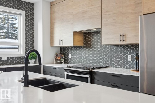 Kitchen with stainless steel appliances, light stone counters, dual tone cabinetry, tasteful backsplash, and modern cabinets - 11016 132 Street, Edmonton, AB - Indoor Photo Showing Kitchen With Stainless Steel Kitchen With Double Sink With Upgraded Kitchen