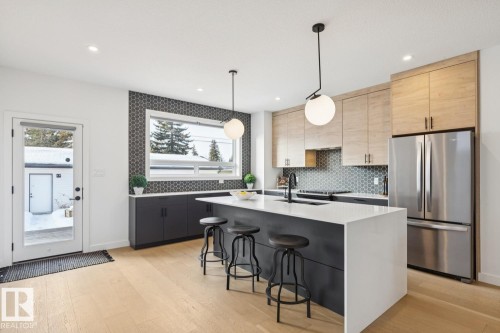 Kitchen featuring freestanding refrigerator, a kitchen breakfast bar, hanging light fixtures, an island with sink, and light stone countertops - 11016 132 Street, Edmonton, AB - Indoor Photo Showing Kitchen With Stainless Steel Kitchen With Upgraded Kitchen