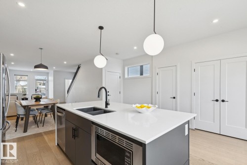 Kitchen featuring decorative light fixtures, stainless steel appliances, a center island with sink, light wood-style floors, and light stone countertops - 11016 132 Street, Edmonton, AB - Indoor Photo Showing Kitchen With Double Sink With Upgraded Kitchen
