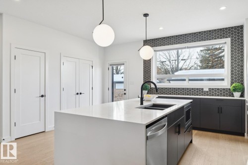 Kitchen featuring decorative light fixtures, a kitchen island with sink, dark cabinetry, and light stone countertops - 11016 132 Street, Edmonton, AB - Indoor Photo Showing Kitchen With Double Sink