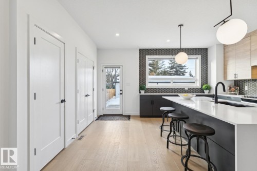 Kitchen with a kitchen bar, decorative backsplash, light wood-style flooring, light stone counters, and decorative light fixtures - 11016 132 Street, Edmonton, AB - Indoor Photo Showing Kitchen